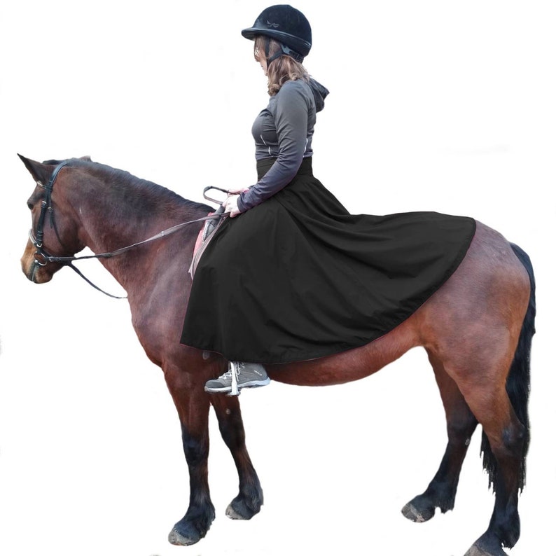 May include: A black riding skirt covers the horse and rider. The skirt is made of a flowing fabric. The horse is a dark brown color and is wearing a bridle. The rider is wearing a black helmet and a gray jacket.