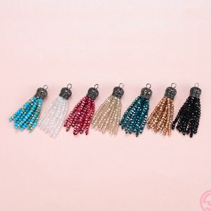 May include: Eight colorful beaded tassels with metal tops. The tassels are in shades of turquoise, white, red, beige, teal, gold, black, and white.