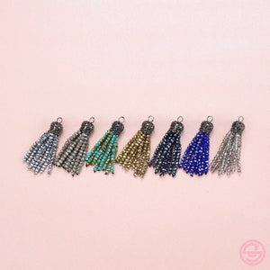 May include: Eight beaded tassels in various colors, including silver, beige, turquoise, gold, dark blue, light blue, and clear. Each tassel has a metal top with a decorative design.