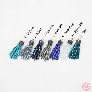May include: Seven different colored crystal tassel charms with silver metal tops. The tassels are in the colors sky blue, silver, dark blue, gray, royal blue, clear crystal, and teal.