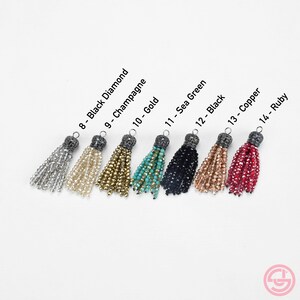 May include: Eight tassel charms in different colors, including black diamond, champagne, gold, sea green, black, copper, and ruby. Each tassel has a silver-toned metal top with a decorative design.