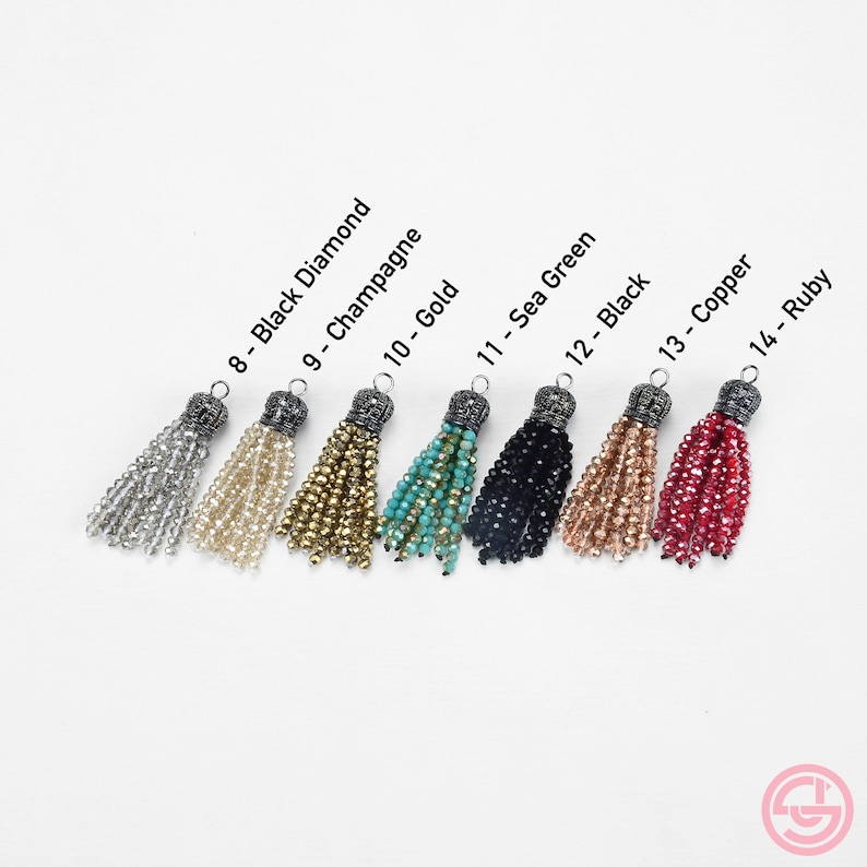 May include: Eight tassel charms in different colors, including black diamond, champagne, gold, sea green, black, copper, and ruby. Each tassel has a silver-toned metal top with a decorative design.