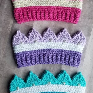 May include: Three handmade crochet crowns in pink, purple, and teal. Each crown features a scalloped edge and is adorned with faux pearls. The crowns have a ribbed band and are suitable for children.