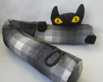 May include: Black and white checked doorstop shaped like a cat with yellow eyes. The cat is lying down with its head and paws sticking out.
