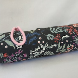 Può includere: Un tubo in tessuto nero con una stampa floreale in tonalità rosa, rosso, blu e bianco. Il tubo ha un elastico rosa a un'estremità.