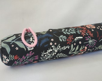May include: A black fabric tube with a floral print in shades of pink, red, blue, and white. The tube has a pink elastic band at one end.