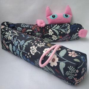 Può includere: Un astuccio per matite in tessuto con motivo floreale bianco e nero con un cinturino in tessuto rosa. Un gatto rosa con gli occhi blu è sdraiato sopra l'astuccio.