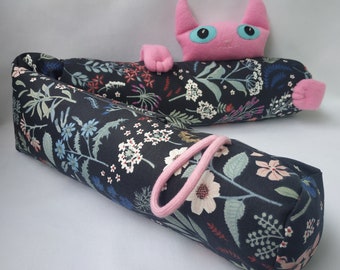 Può includere: Un astuccio per matite in tessuto con motivo floreale bianco e nero con un cinturino in tessuto rosa. Un gatto rosa con gli occhi blu è sdraiato sopra l'astuccio.