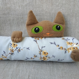 以下が含まれることがあります： 緑色の目をした茶色の猫の形をしたドアストッパー。薄い青色の花柄の布地のボディです。