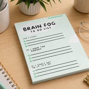 May include: A rectangular notepad with a light green grid background and white cloud graphics. The text reads BRAIN FOG TO DO LIST, TOP 3 TASKS, IF I HAVE THE ENERGY, and IF I CAN'T GET TO IT, IT'S OK, with black lines and green circular bullet points.