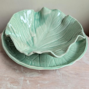 May include: A set of two green ceramic bowls shaped like cabbage leaves. The bowls are nested together.