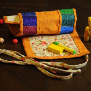 May include: A colorful fabric roll-up pouch with a floral pattern and a yellow eraser. The pouch has a tie closure and is perfect for storing small items.
