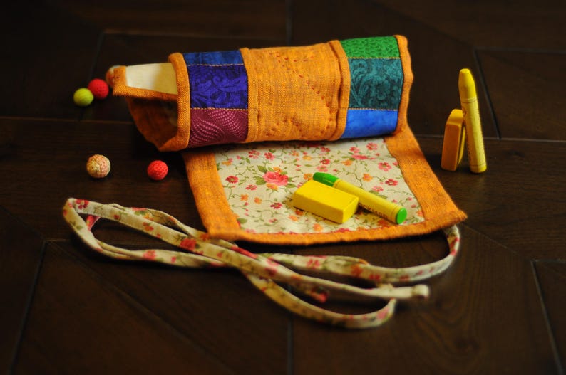 May include: A colorful fabric roll-up pouch with a floral pattern and a yellow eraser. The pouch has a tie closure and is perfect for storing small items.