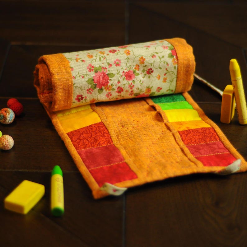 May include: A rolled-up fabric pencil case with a floral print on the outside and a rainbow of colors on the inside. The case is made of a patchwork of different fabrics and is unzipped.