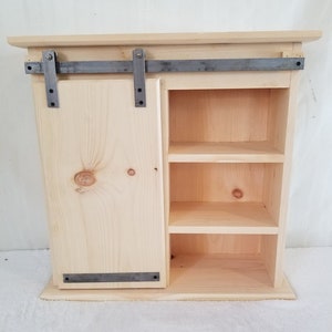 Unfinished Sliding Barn Door Cabinet. Measures: 26" x 9 1/4" x 25 1/2".  Door Slides on Metal Rail.