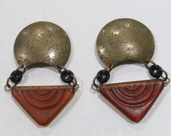 May include: A pair of gold and amber earrings with a crescent moon shape and a triangular bottom. The earrings have a textured gold finish and a carved amber design.
