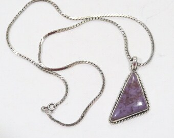 May include: A silver necklace with a triangular pendant. The pendant features a purple stone with a silver rope-like border. The chain is a flat, linked design. The necklace is displayed on a white surface.