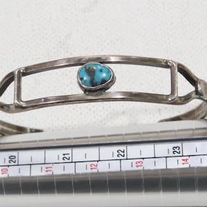 Puede incluir: Una pulsera de plata con una piedra turquesa engastada en un marco rectangular. La pulsera tiene aproximadamente 5 cm de ancho y un diseño sencillo.