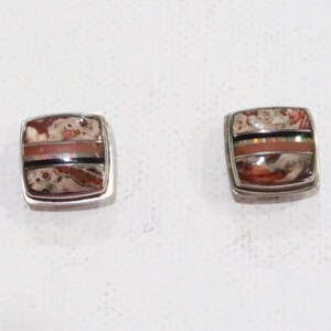 May include: A pair of square stud earrings with a silver border. Each earring features a mosaic design with a mix of brown, red, black, and white tones. The earrings are set against a white background.