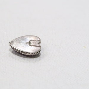 May include: A small, silver-colored heart-shaped pendant. The pendant has a textured surface and a decorative rope-like border. A small loop is attached to the top for hanging. The pendant is likely made of metal and is suitable for jewelry making.
