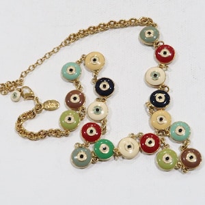 May include: A gold chain necklace with multiple colorful eye charms. The charms are round and have a gold rim with a white pupil and a black outline. The charms are in various colors, including blue, green, red, yellow, and brown.