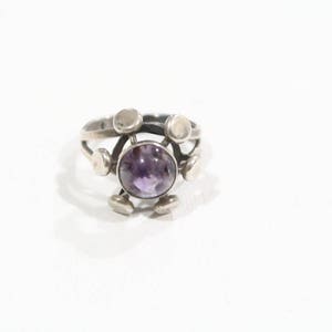 Könnte beinhalten: Ein silberner Ring mit einem violetten Amethyst-Edelstein, der in einem geometrischen Design gefasst ist.
