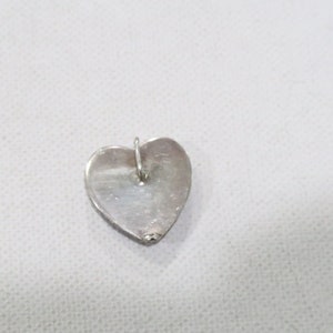 May include: A silver heart-shaped pendant with a small loop at the top for a chain. The pendant is smooth and shiny, reflecting the light. The heart is approximately 0.75 inches wide and 0.75 inches tall.