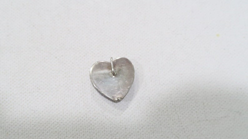 May include: A silver heart-shaped pendant with a small loop at the top for a chain. The pendant is smooth and shiny, reflecting the light. The heart is approximately 0.75 inches wide and 0.75 inches tall.