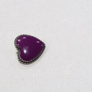 May include: A heart-shaped purple brooch with a silver-colored rope-like border. The brooch is set against a white background. The heart is a solid, glossy purple color.