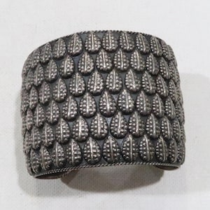 May include: A silver bracelet with a textured design of repeating teardrop shapes.