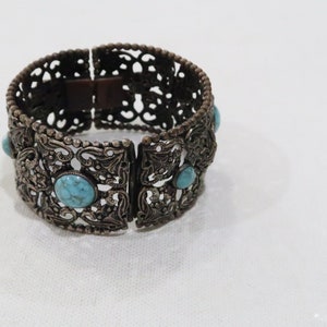 Puede incluir: Un brazalete de plata con un diseño de filigrana y piedras turquesa.
