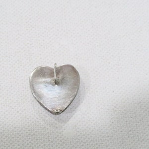May include: A silver heart-shaped pendant with a small loop at the top for a chain. The pendant has a smooth, polished surface and is likely made of sterling silver. The heart shape is clearly defined.