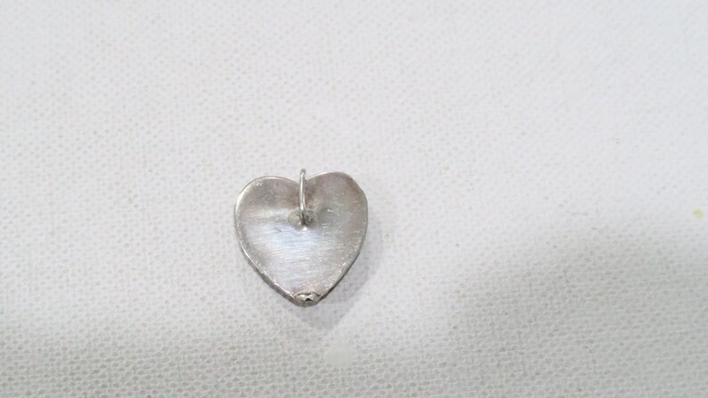May include: A silver heart-shaped pendant with a small loop at the top for a chain. The pendant has a smooth, polished surface and is likely made of sterling silver. The heart shape is clearly defined.