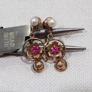 May include: A pair of gold tone clip-on earrings with pink flower accents and pearl tops.