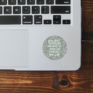 May include: A green and white sticker with a quote that reads "You don't understand now what I'm doing but someday you will."  The quote is written in a handwritten style with a floral design around the text.