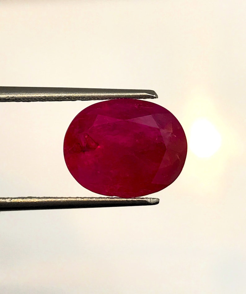 以下が含まれることがあります： 丸くファセットカットされた、鮮やかな深紅色のルビーの宝石。ルビーはピンセットで固定されています。