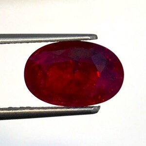 Puede incluir: Una piedra preciosa de rubí ovalada de color rojo oscuro sostenida por unas pinzas.
