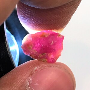 Pode incluir: Uma gema de rubi rosa vibrante com uma forma natural e áspera. O rubi é segurado na mão, mostrando sua cor e textura.