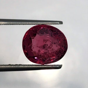 Puede incluir: Una piedra preciosa ovalada de color rosa sostenida por unas pinzas.