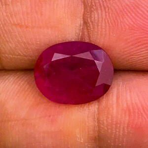 以下が含まれることがあります： ファセットカットされた深紅のルビーの宝石。宝石は楕円形で、高い光沢があります。