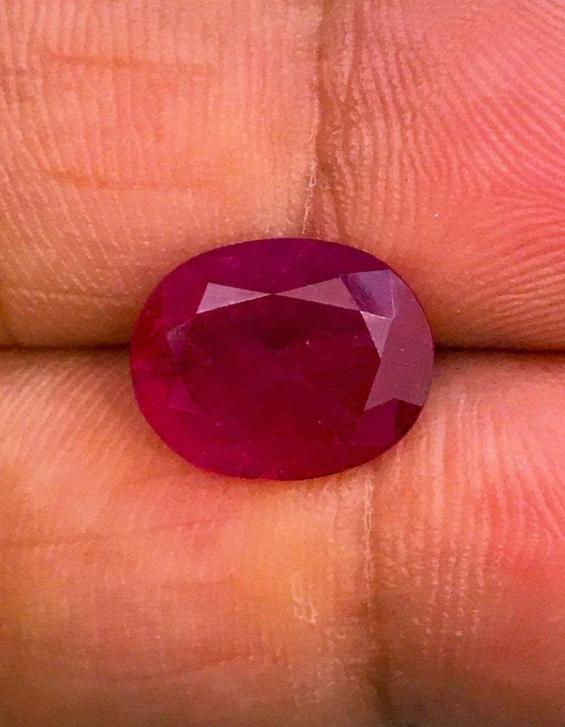 以下が含まれることがあります： ファセットカットされた深紅のルビーの宝石。宝石は楕円形で、高い光沢があります。