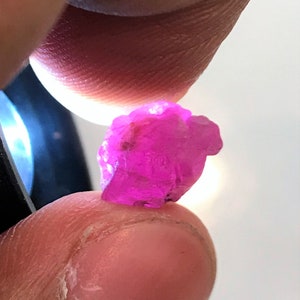 Puede incluir: Una gema rosa vibrante con una forma natural y rugosa. La gema se sostiene en una mano, mostrando su tamaño y color.