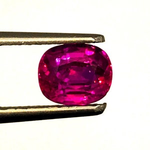 Może przedstawiać: Owalny, żywy różowy kamień szlachetny trzymany przez pęsetę.