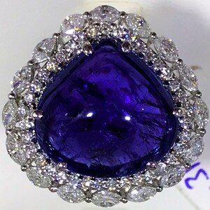 May include: A large, deep blue gemstone ring with a pear-shaped center stone surrounded by a halo of smaller, clear gemstones.