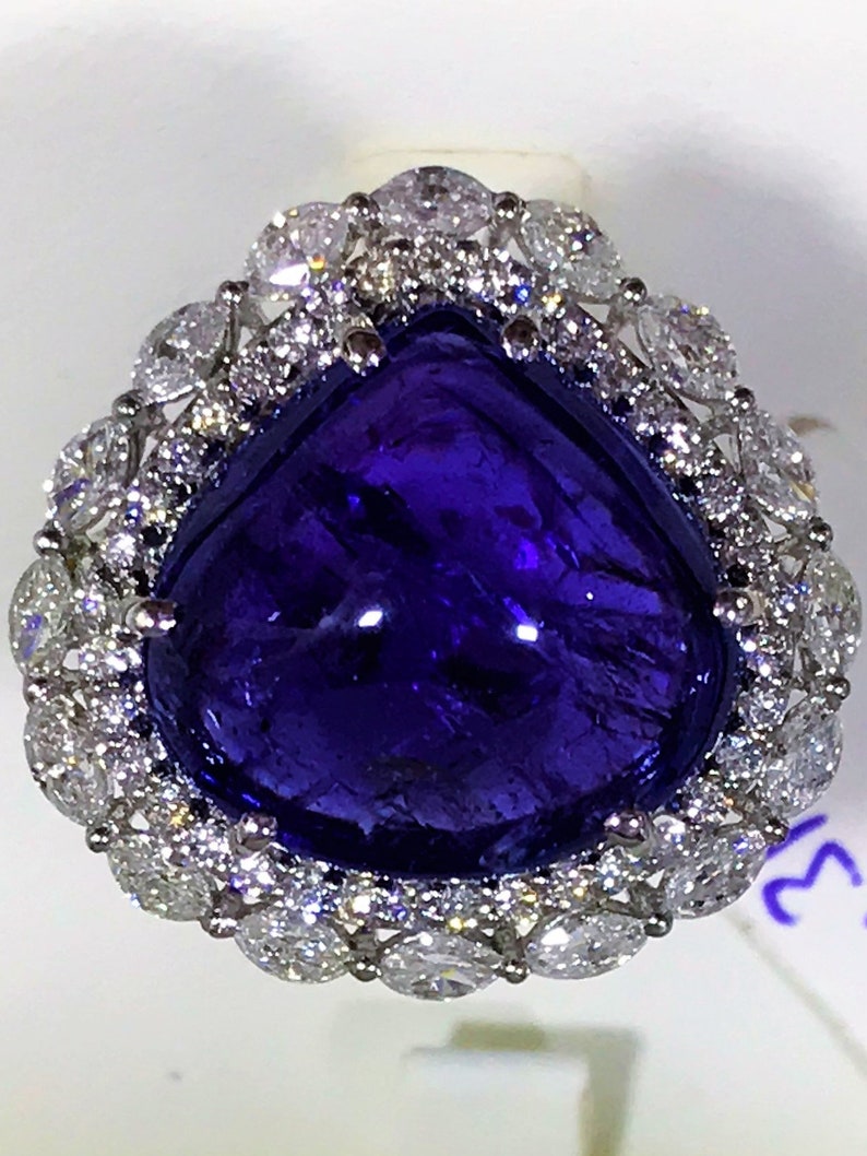 May include: A large, deep blue gemstone ring with a pear-shaped center stone surrounded by a halo of smaller, clear gemstones.
