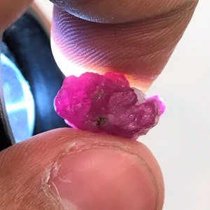 Puede incluir: Primer plano de una piedra preciosa de rubí rosa. El rubí es áspero y tiene un aspecto natural sin pulir.