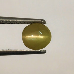 May include: A round, yellow-green gemstone with a chatoyant effect, held in tweezers.