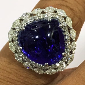 May include: A large, deep blue gemstone ring with a halo of smaller, clear gemstones. The ring is set in a white metal band.