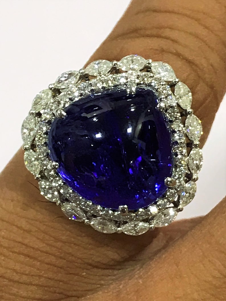 May include: A large, deep blue gemstone ring with a halo of smaller, clear gemstones. The ring is set in a white metal band.
