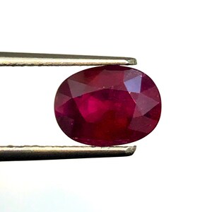 Pode incluir: Uma gema oval de cor vermelha escura mantida por pinças. A gema é um rubi.